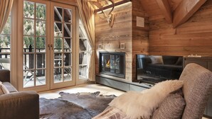 Ein Holzblockhaus-Innenraum mit Kamin, Fernseher und einem großen Fenster mit Vorhängen.