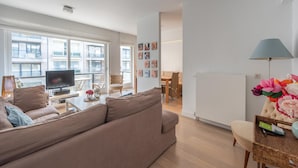 Un salon moderne comprenant un canapé, un téléviseur et un coin repas avec des chaises et une table.