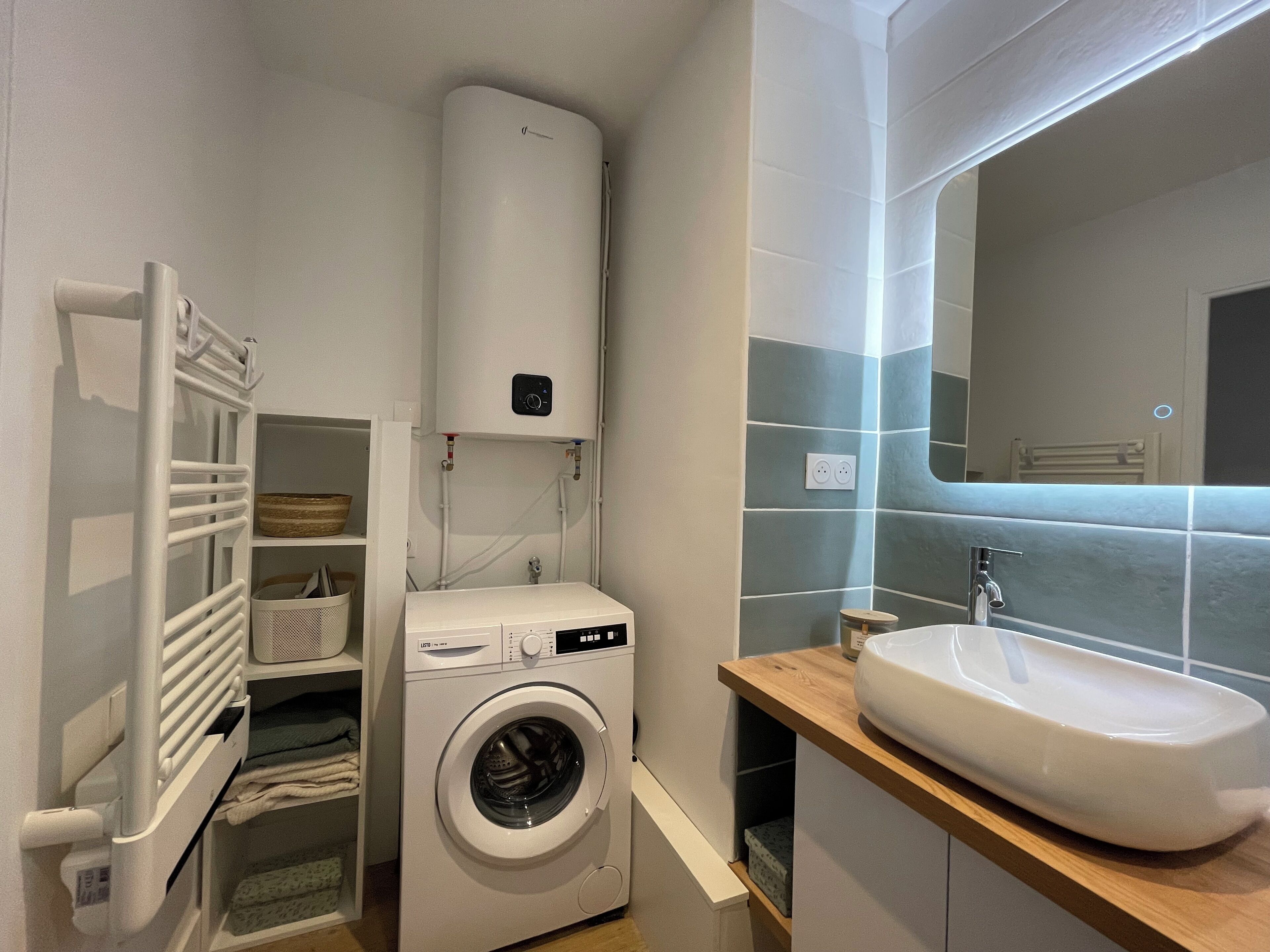 Une petite buanderie équipée d’un lave-linge à chargement frontal, d’un radiateur encastré et d’un évier doté d’un plan de travail en bois.