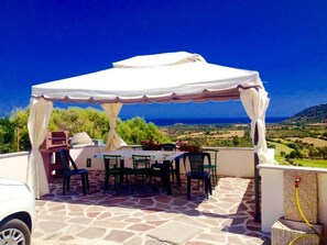 Eine Terrasse im Freien mit überdachtem Tisch und Stühlen, einem Grill und einer schönen Landschaftsaussicht.