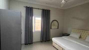 A bedroom with a bed, a wardrobe, a ceiling fan, and a window with curtains.
