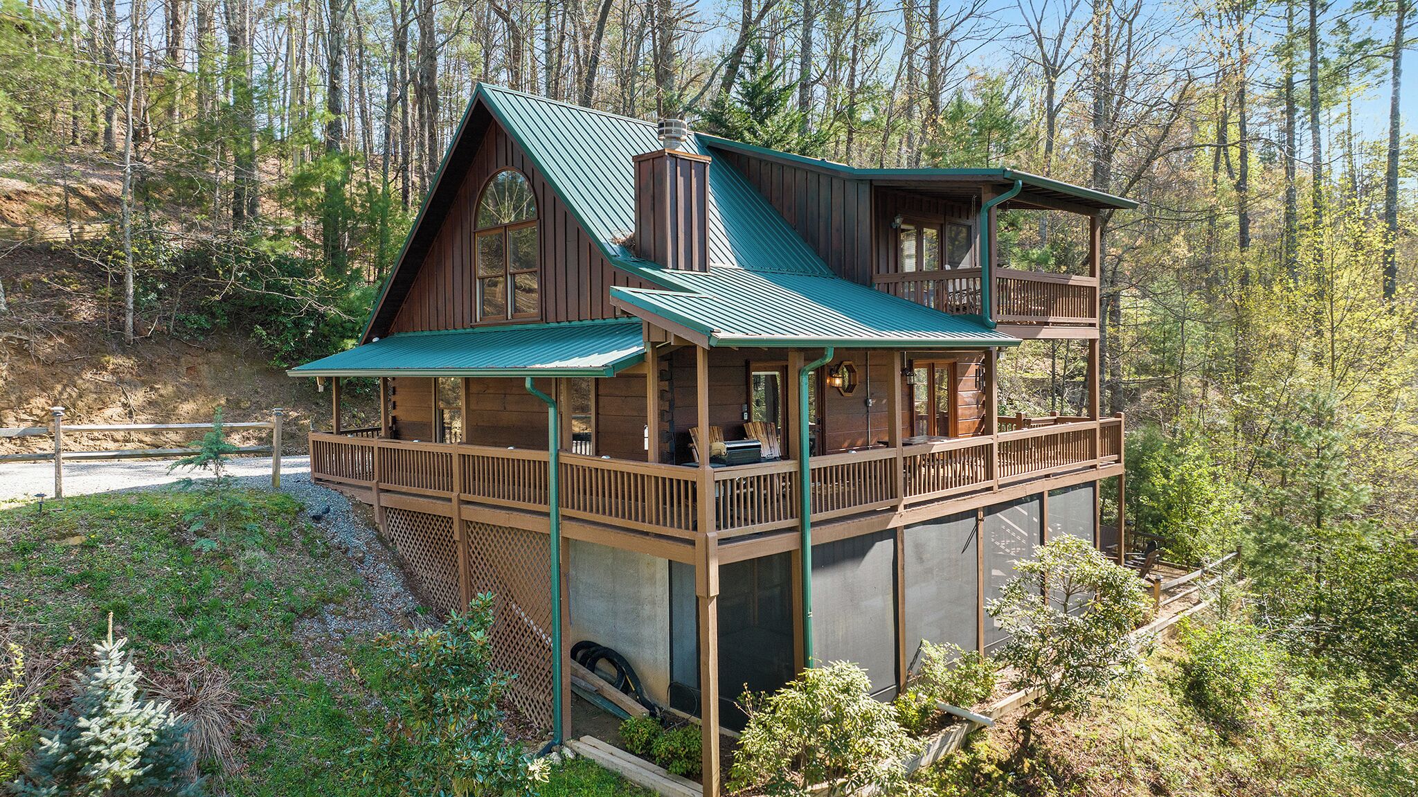 A two-story cabin with a balcony, surrounded by forest.