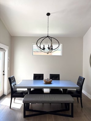 Un coin repas comprenant une table rectangulaire, quatre chaises, un banc et un lustre.