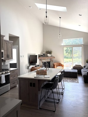 Una cocina moderna con una isla central, comedor con sillas, un televisor y una chimenea.