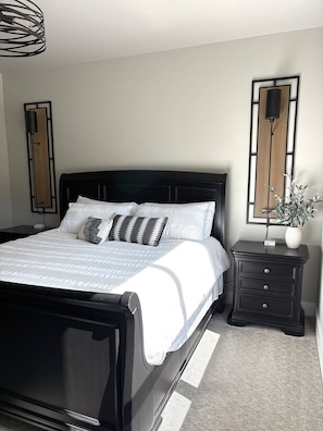 Un dormitorio moderno con un cabecero negro, ropa de cama blanca y dos mesitas de noche con lámparas.