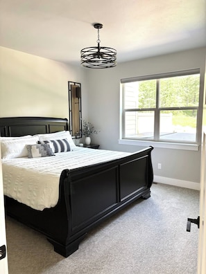 Une chambre avec un lit noir, une grande fenêtre et un luminaire au plafond.