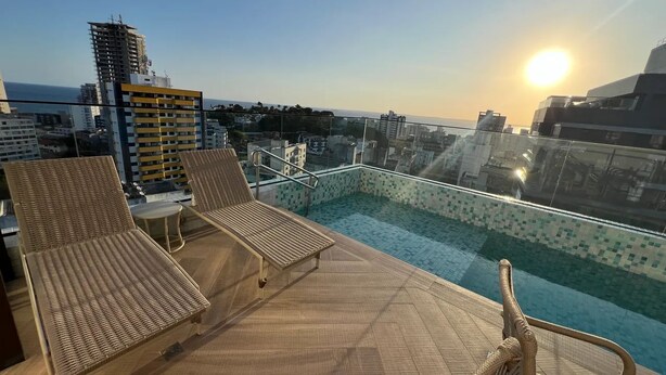 A rooftop pool with lounge chairs and a glass balustrade overlooking a cityscape.