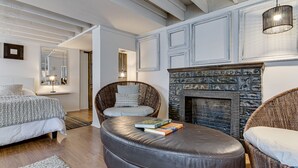 Een moderne woonkamer met een open haard, een leren poef en rieten stoelen.