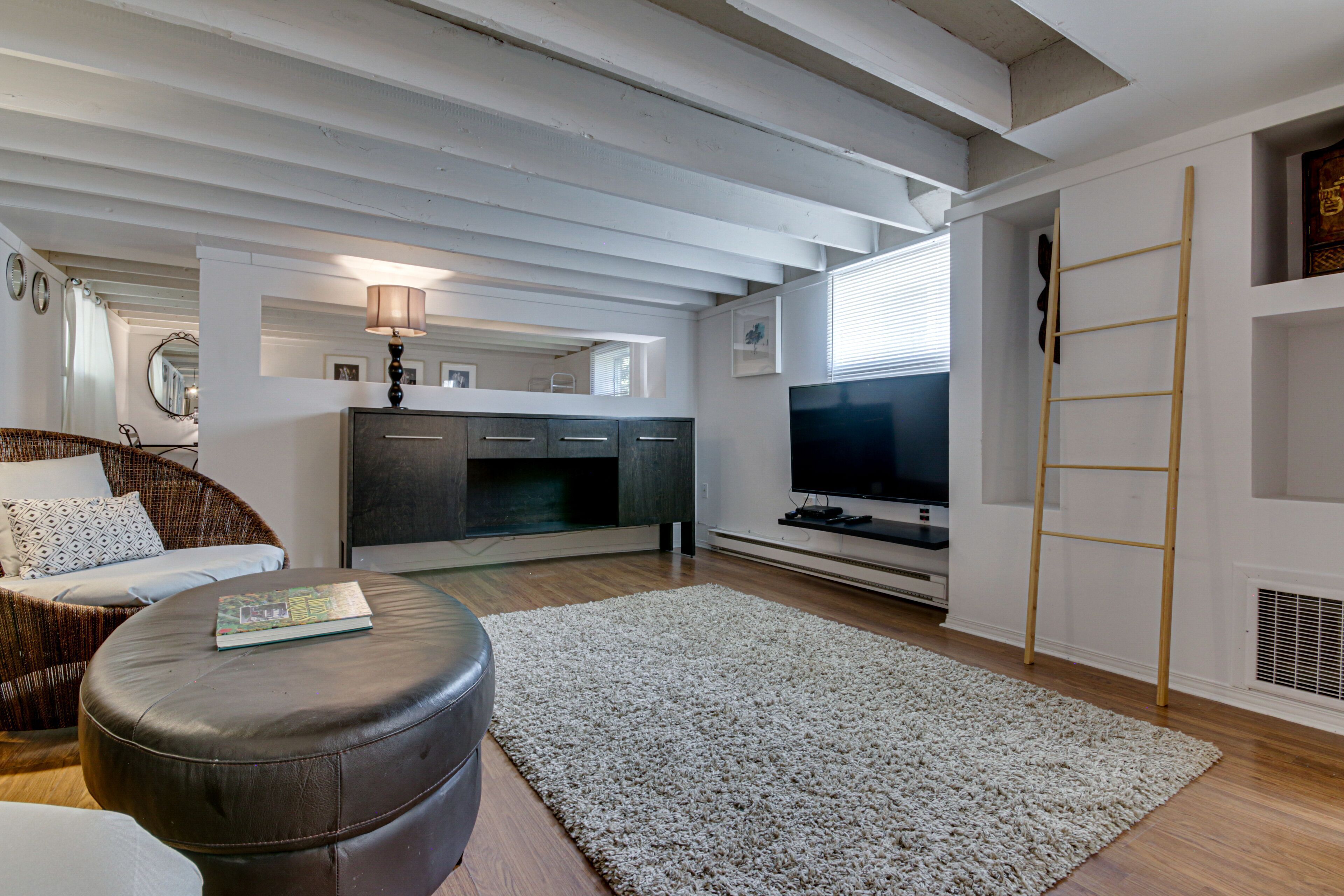 Ein modernes Wohnzimmer mit Sofa, Hocker, Fernseher und Kamin.