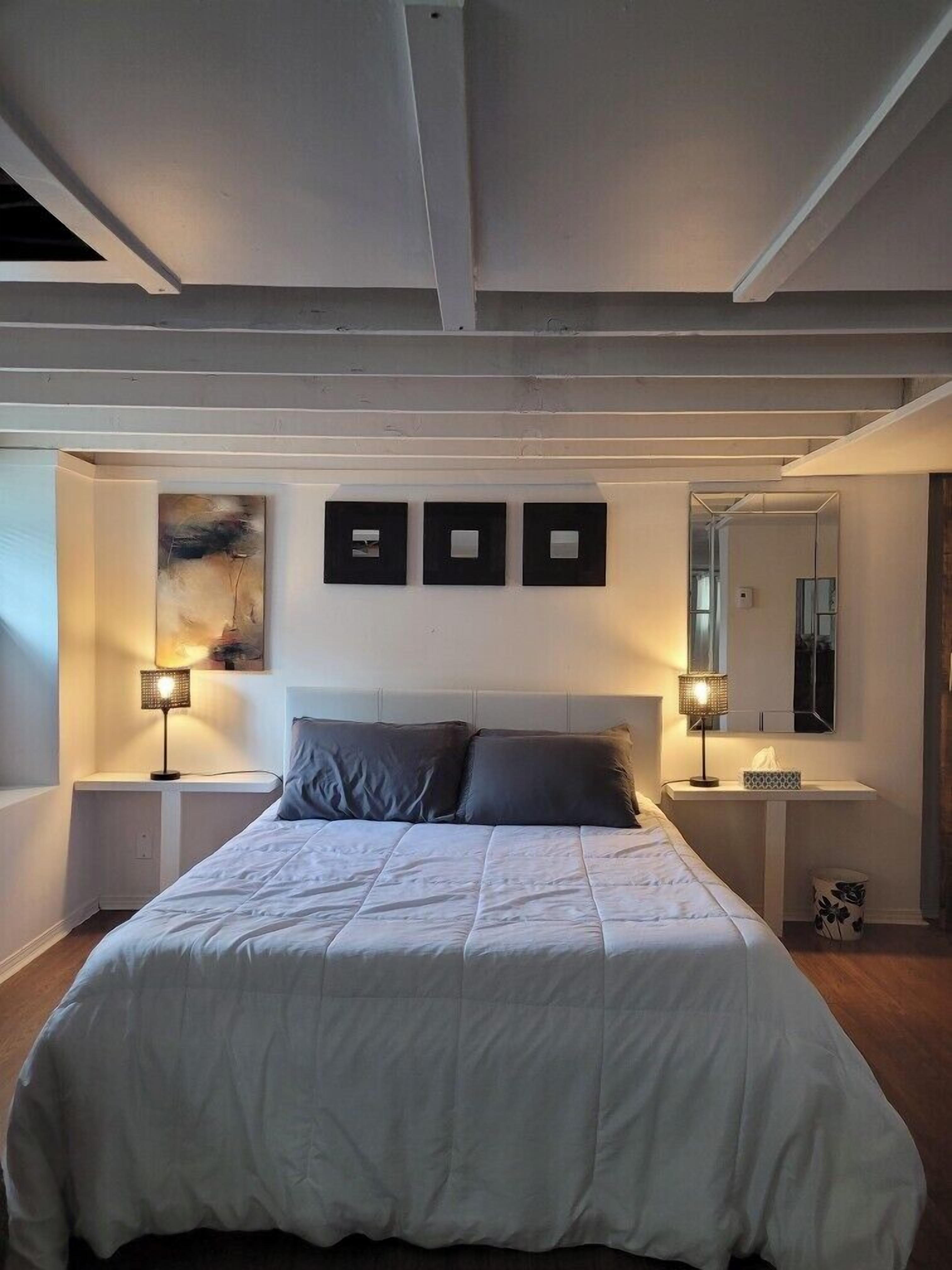 Un dormitorio con una cama grande, dos mesitas de noche con lámparas, un cabecero y un espejo en la pared.