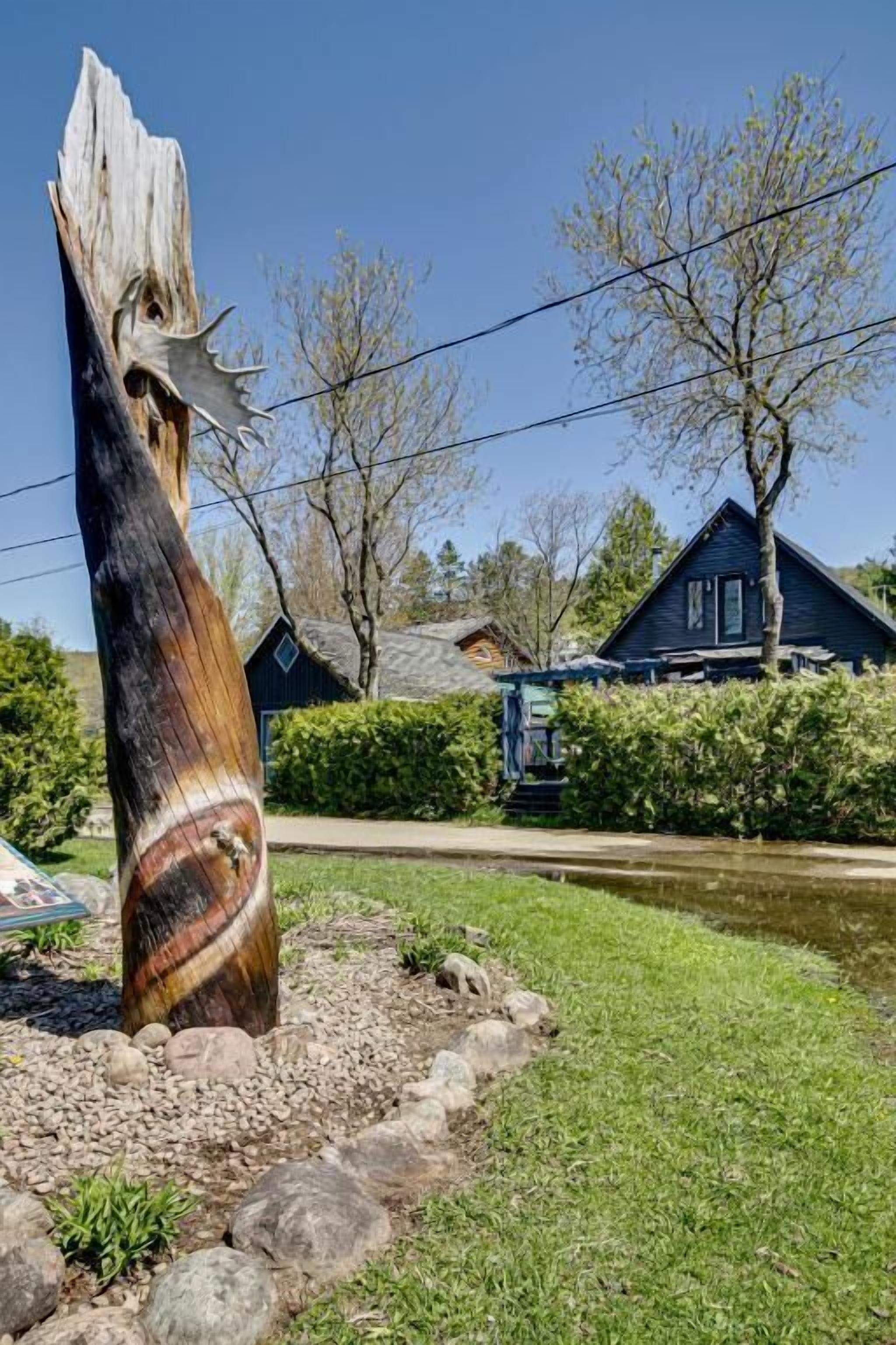 A rustic wooden sculpture in a landscaped area with a house in the background.