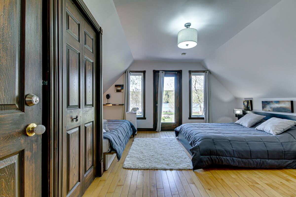 Un dormitorio con dos camas, piso de madera, alfombra blanca y una lámpara en el techo.