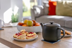 A table with a teapot, a bowl of fruit, and a plate of scones.