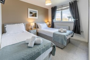 Une chambre d’hôtel avec deux lits, une fenêtre avec des rideaux, un tableau au mur et une lampe sur la table de chevet.