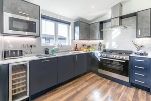 A modern kitchen with a built-in microwave, stainless steel appliances, and a large window providing natural light. - 3 Bed in Broadwoodwidger (oc-s31783) (Broadwoodwidger)