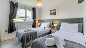 Habitación de hotel con dos camas, una ventana con cortinas, una mesita de noche con lámpara y un cuadro en la pared.