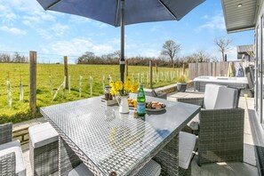 An outdoor patio with a table set for two, featuring a bottle of Pellegrino water, a pitcher, and a plate of food. - 3 Bed in Broadwoodwidger (oc-s31783) (Broadwoodwidger)