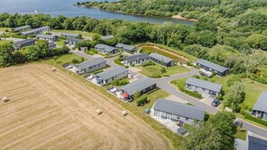 A residential area with modern houses, a large open field, and a lake in the background. - 3 Bed in Broadwoodwidger (oc-h31771) (Broadwoodwidger)