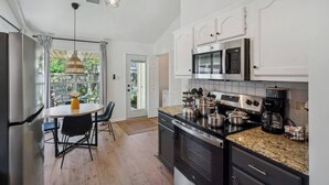 Una cocina moderna con armarios blancos, electrodomésticos de acero inoxidable y un comedor con mesa y sillas.