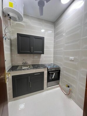 A compact kitchen with a built-in stove, a sink, and black cabinets. - Red 8 - OKAAD (Salalah)