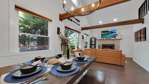 A dining area with a long wooden table, blue placemats, and a fireplace in the background. - Lakefront | Hot Tub | Kayaks | High End | Peaceful (Tobyhanna)