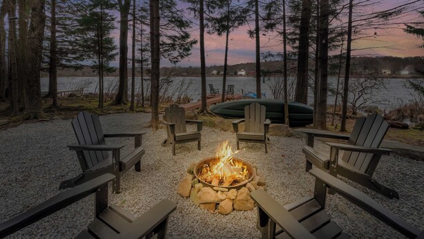 A fire pit surrounded by Adirondack chairs, a lake view, and a dock with a boat. - Lakefront | Hot Tub | Kayaks | High End | Peaceful (Tobyhanna)