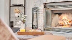 A cozy living room with a fireplace, a tray with breakfast items, and a bookshelf. - Lakefront | Hot Tub | Kayaks | High End | Peaceful (Tobyhanna)