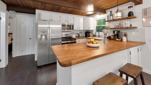 A modern kitchen with white cabinets, stainless steel appliances, a wooden island with stools, and hanging pendant lights. - Lakefront | Hot Tub | Kayaks | High End | Peaceful (Tobyhanna)