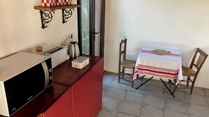 A kitchenette with a microwave, toaster, and coffee maker. There is a small table with a striped tablecloth and two chairs. A shelf with checkered containers is visible on the wall. - Room at the foot of the Rhune (Sare)