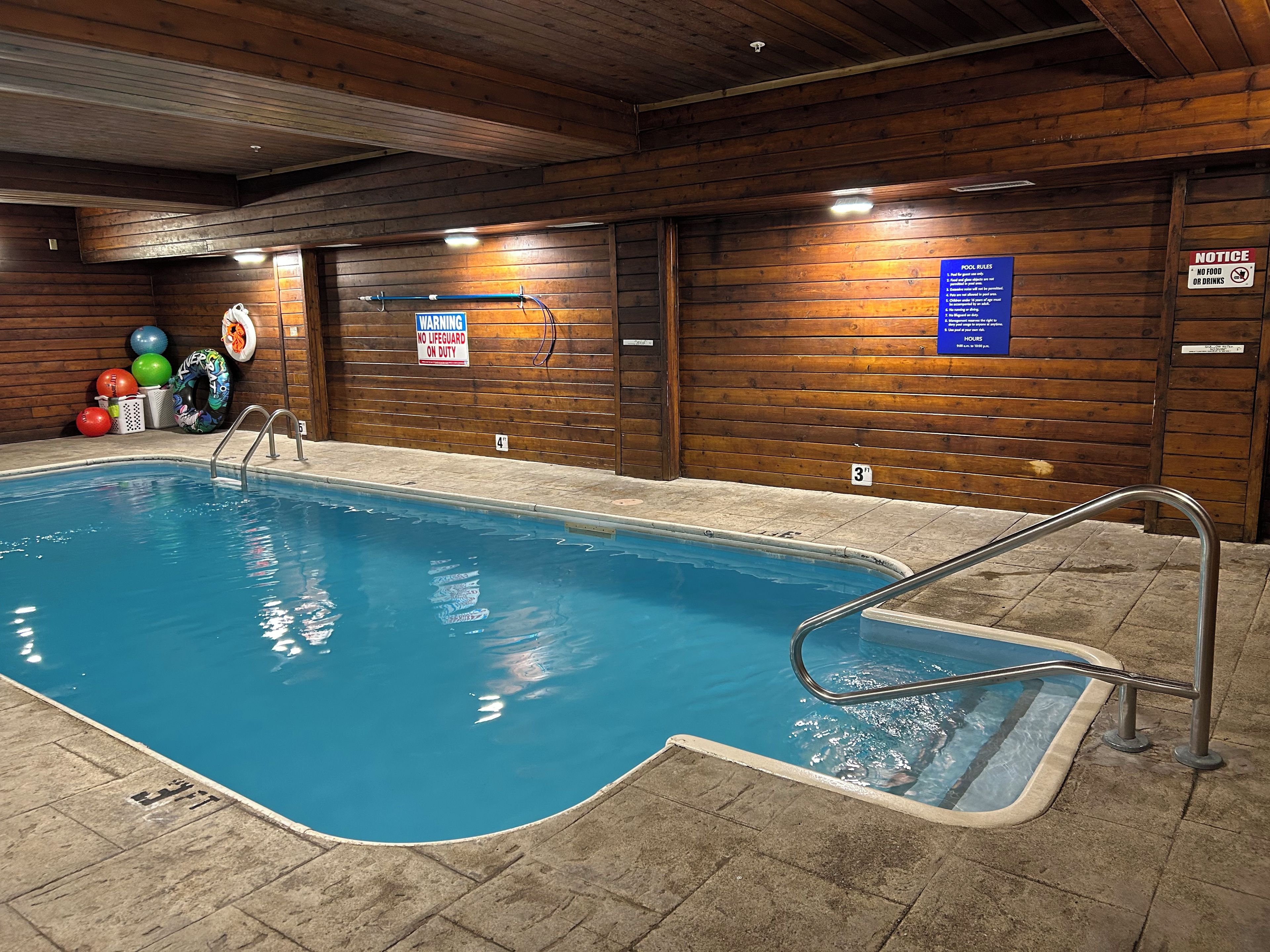 Una piscina interior con una estación de socorristas, un cartel con las normas de la piscina y un aviso.