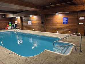 An indoor swimming pool with a lifeguard station, pool rules sign, and a notice sign.