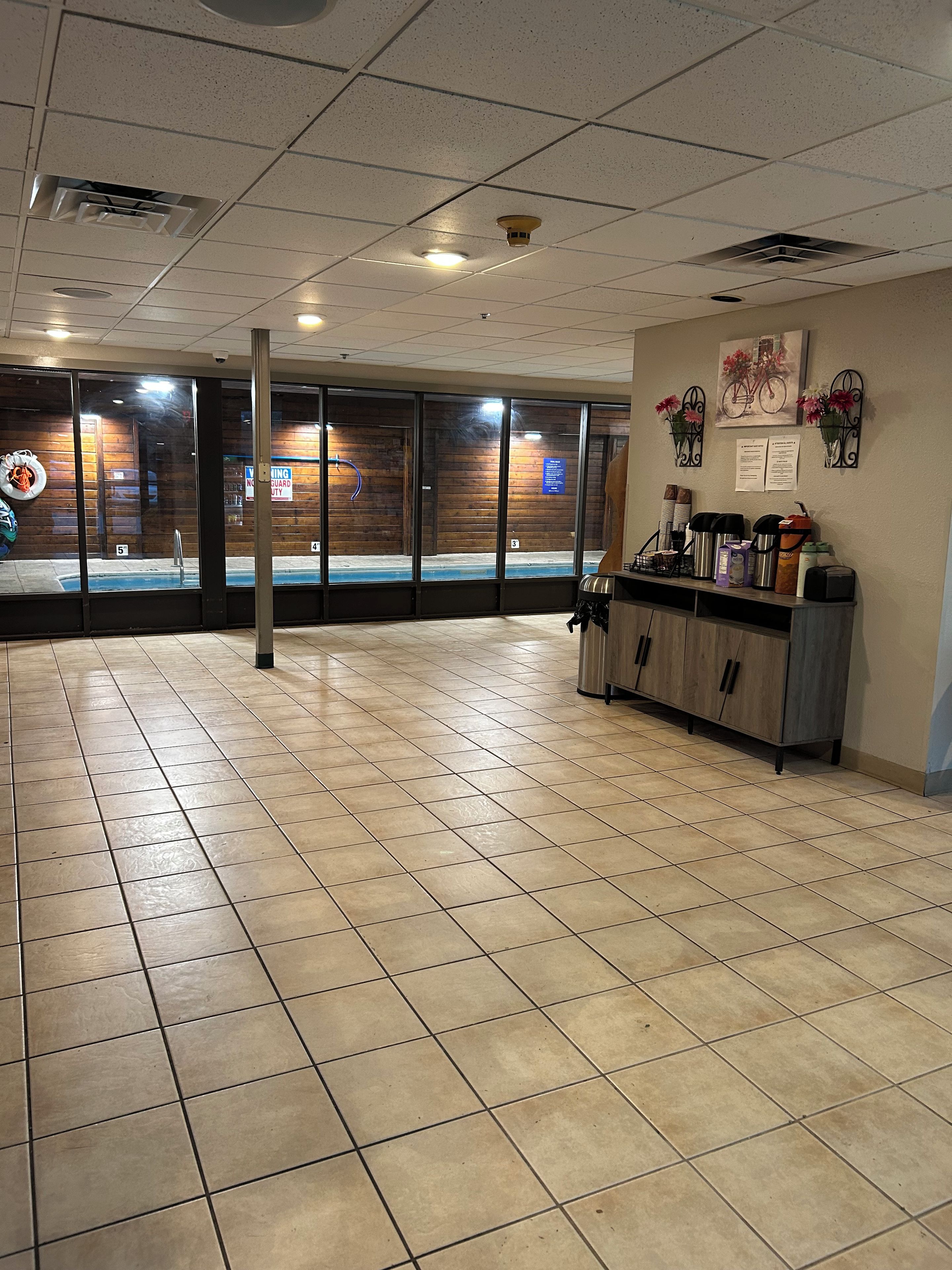 A spacious indoor area with a tiled floor, a reception desk with various items, and a wooden wall with a window.