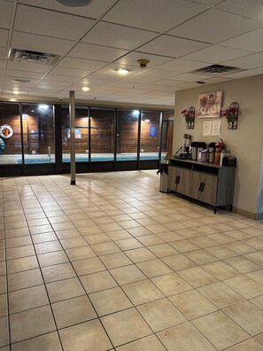A spacious indoor area with a tiled floor, a reception desk with various items, and a wooden wall with a window.