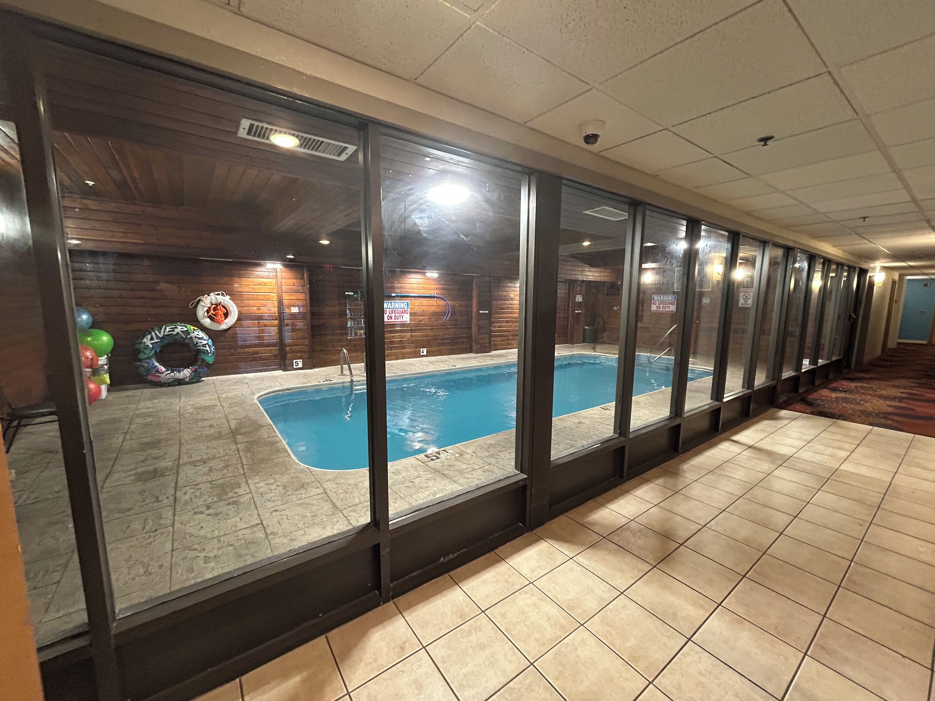 An indoor swimming pool with clear water, surrounded by glass walls, and a tiled floor.