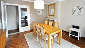 A dining area with a wooden table and chairs, a hanging light fixture, and artwork on the walls. - Apartment in Knokke Near Albertstrand Beach (Knokke-Heist)