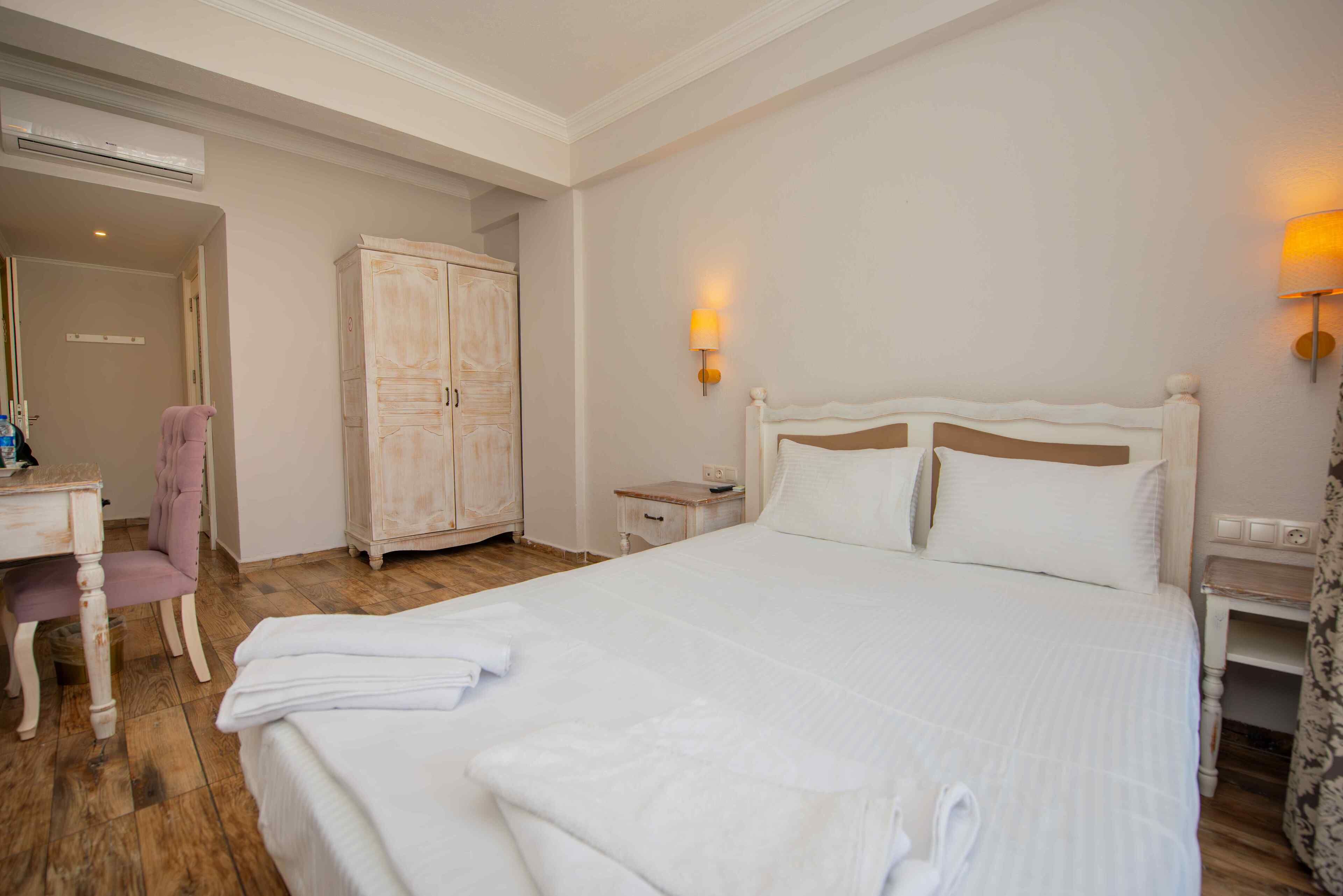 Une chambre d’hôtel avec un grand lit, un bureau, une chaise, une armoire et deux lampes fixées au mur.