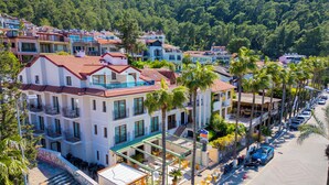 A multi-story hotel with balconies, a ground-level cafe, and a street lined with palm trees. - Cennet Life Boutique Hotel (Fethiye)