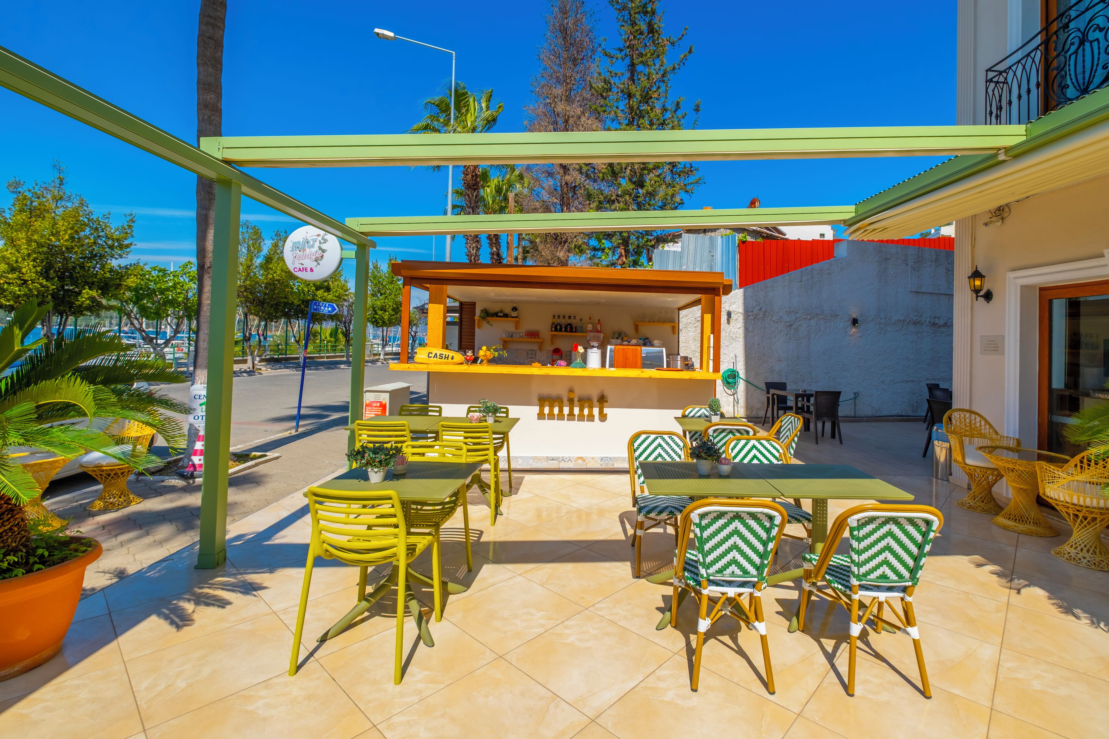 An outdoor cafe with yellow and green chairs, a counter, and a view of the street.