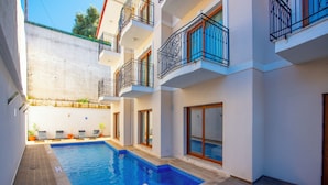 A swimming pool with a wooden deck, surrounded by a white building with balconies and windows. - Cennet Life Boutique Hotel (Fethiye)