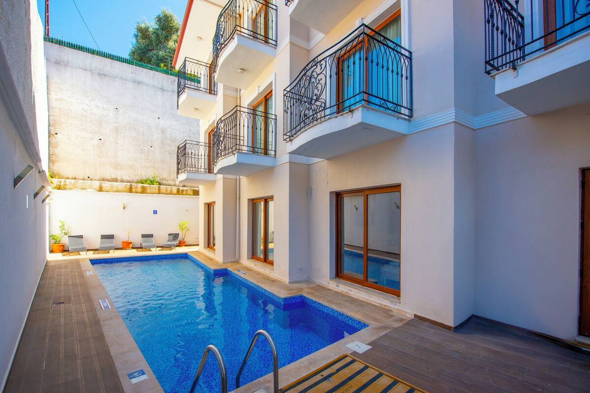 A swimming pool with a wooden deck, surrounded by a white building with balconies and windows.