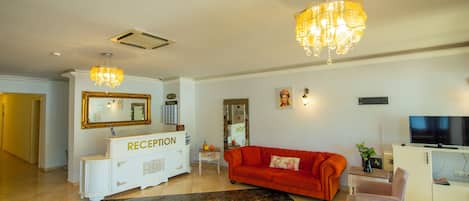 A spacious living area with a reception desk, a red sofa, a television, and a chandelier.