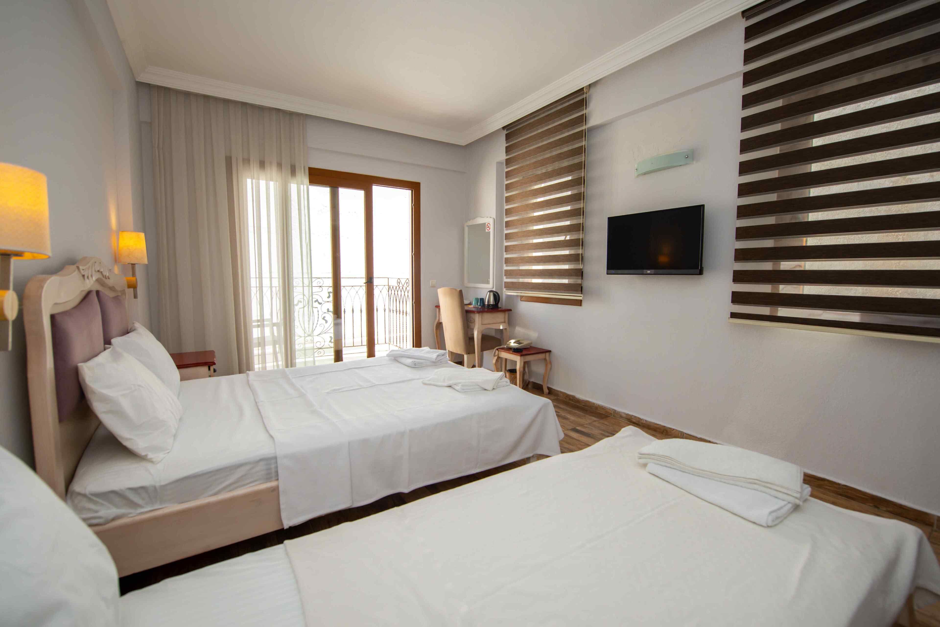 A hotel room with two beds, a desk, a chair, a TV, and a window with blinds.