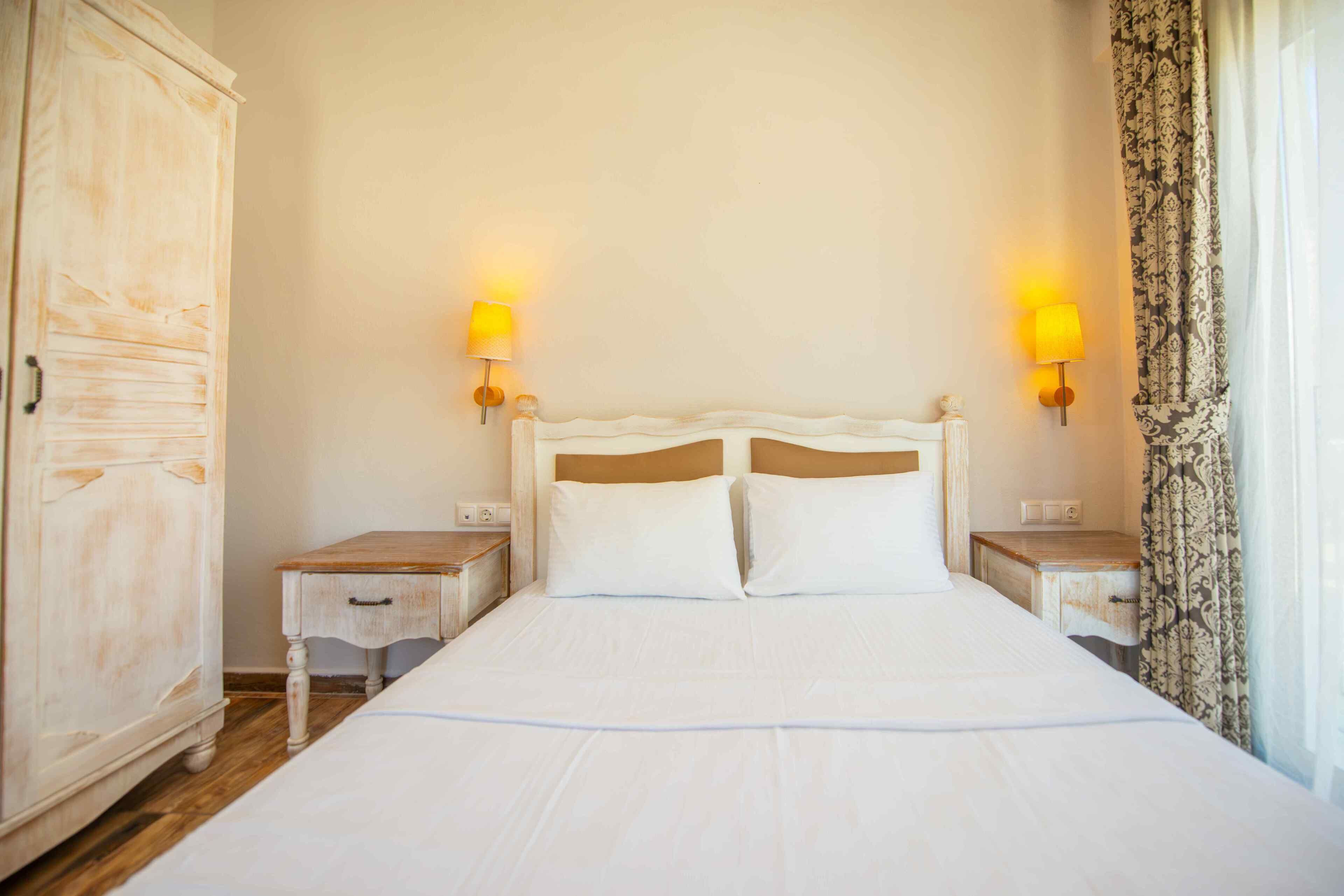 A hotel room with a large bed, two bedside tables, a wardrobe, and two wall-mounted lamps.