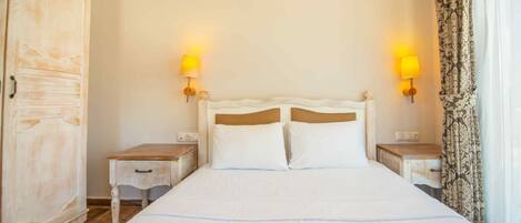 A hotel room with a large bed, two bedside tables, a wardrobe, and two wall-mounted lamps.