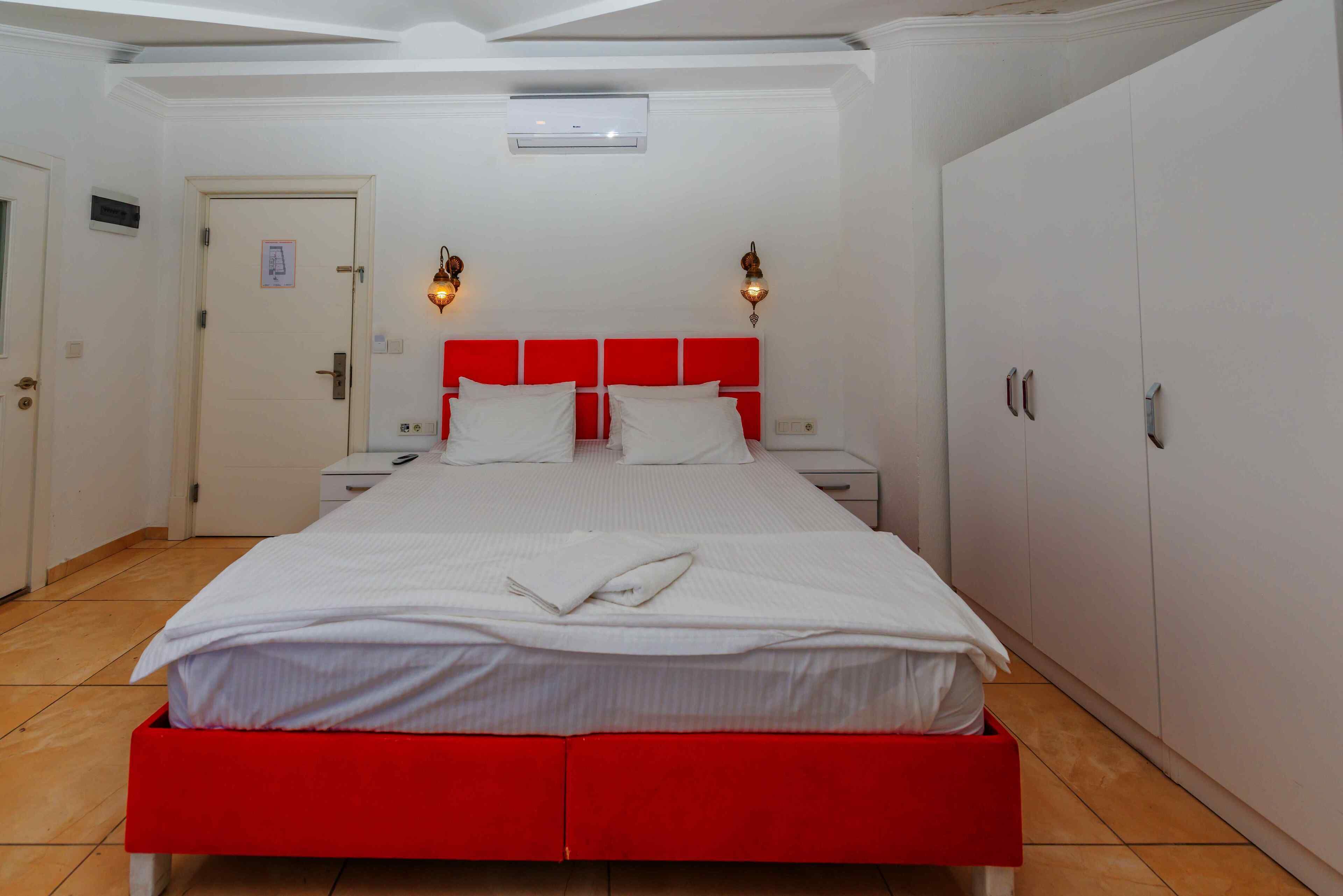 A hotel room with a red bed, white walls, and a white wardrobe.
