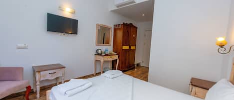 A hotel room with a bed, a TV mounted on the wall, a wooden wardrobe, a small desk with a mirror, and a bedside table.