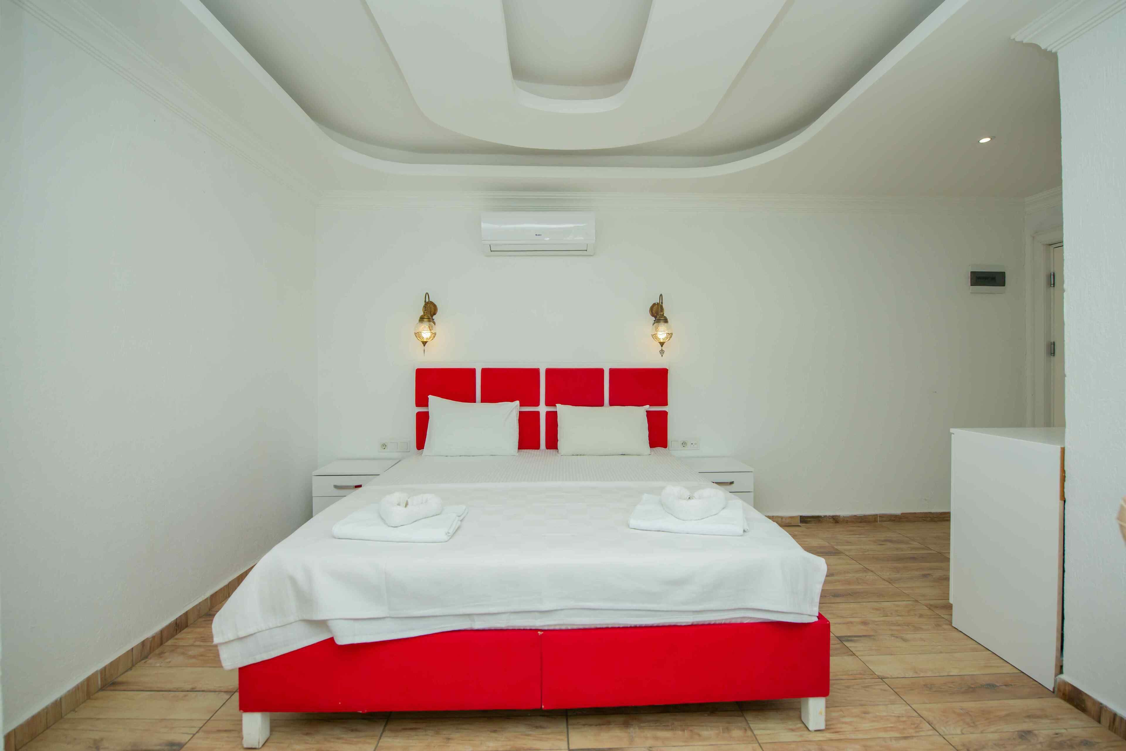 Una habitación de hotel moderna con una cama blanca y roja, paredes blancas e iluminación empotrada en el techo.
