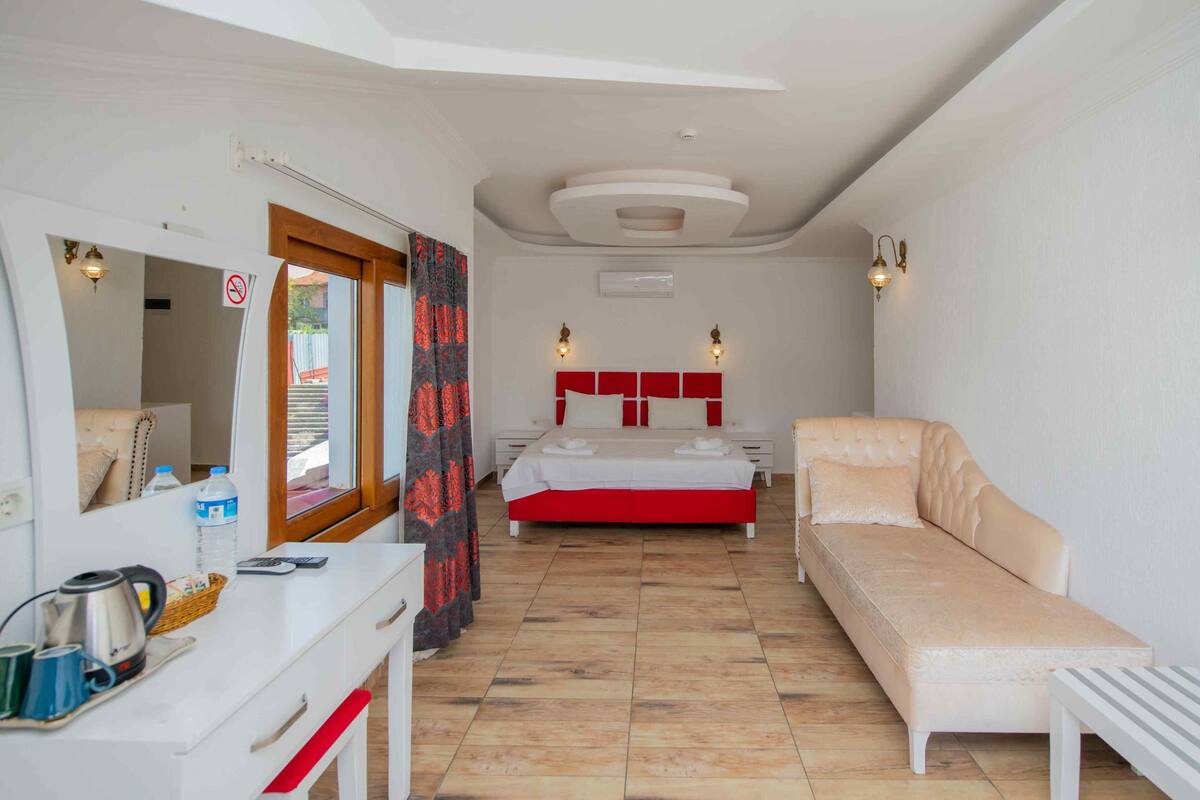 A bedroom with a bed, a sofa, a desk with a kettle, and a mirror.