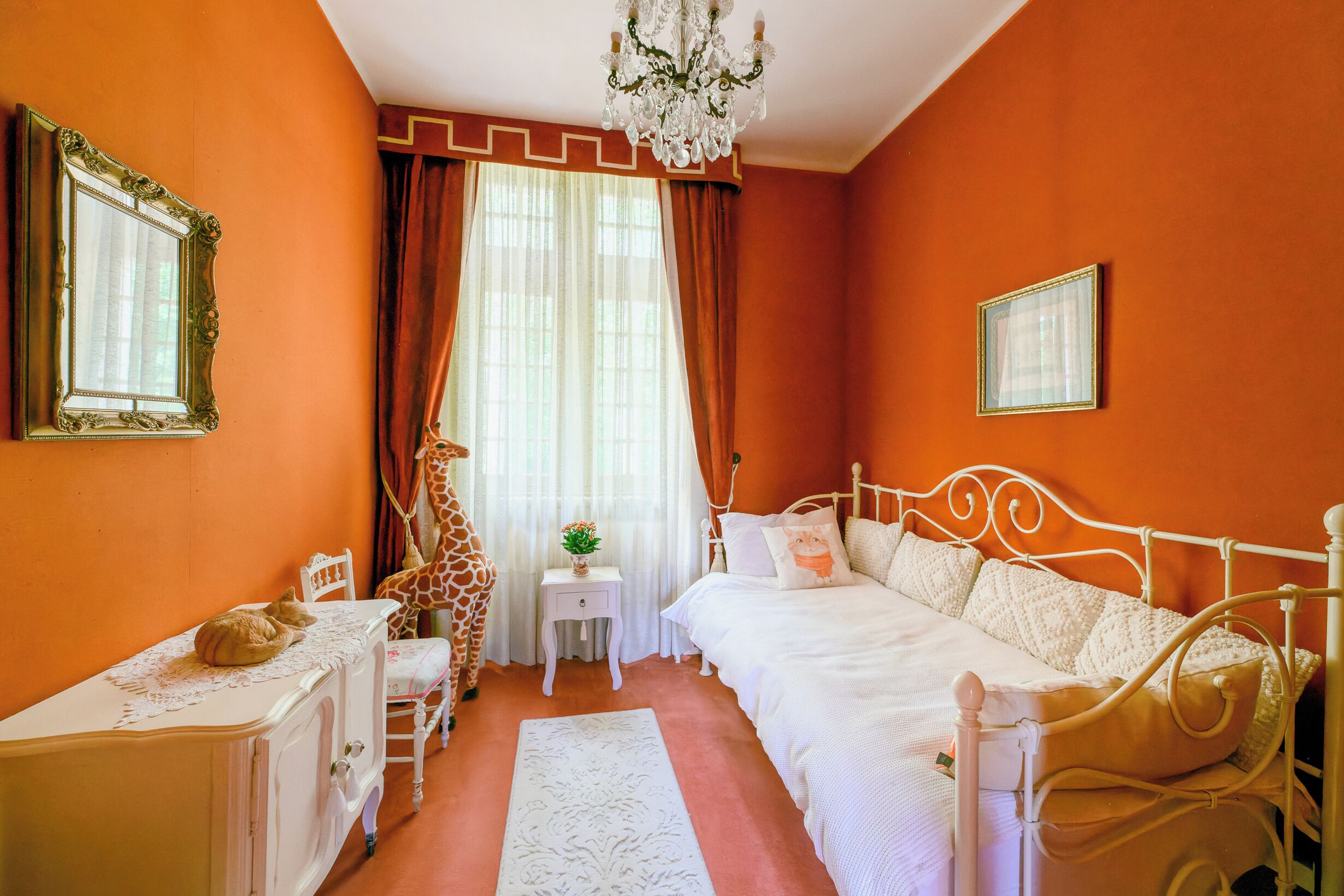 Quarto com cama branca, penteadeira branca, estátua de girafa e um candelabro.
