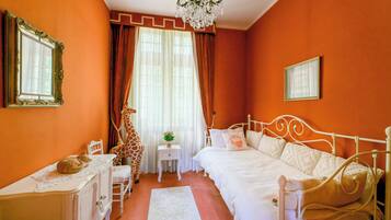 Quarto com cama branca, penteadeira branca, estátua de girafa e um candelabro.
